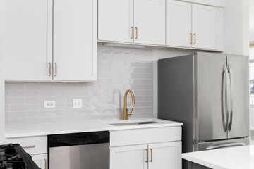 A kitchen detail with white cabinets, gold faucet and hardware, subway tile backsplash, and white quartz countertops. No brands or labels.