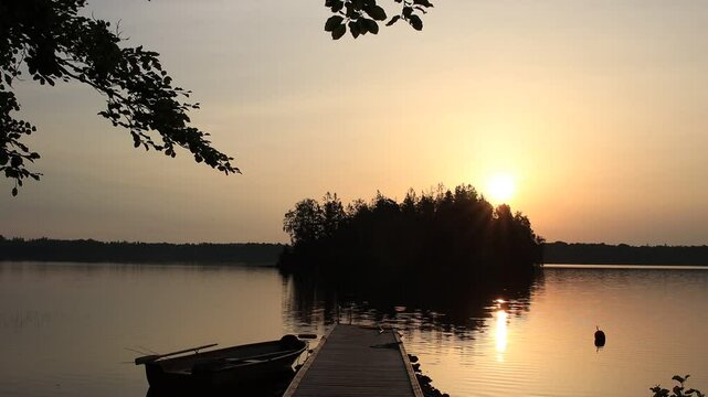 Malerischer Steg mit Ruderboot am Stora Hensj&ouml;n See in Schweden mit Insel und Kraniche die im Hintergrund trompeten.bei Sonnenaufgang.