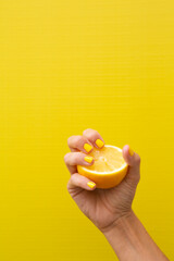 A woman's hand with yellow fingernails squeezing half a lemon