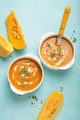 Creamy pumpkin soup bowls on blue background with parsley and pink pepper, a cozy autumn meal option