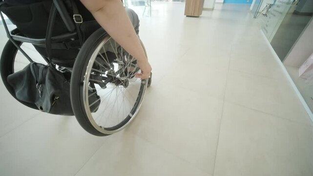 Close-up of a person using a wheelchair indoors, focusing on the wheel and hand as they navigate a smooth, accessible surface.
