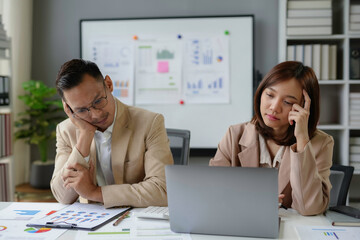 Two businesspeople feeling stressed and tired while working on business report in office