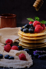 pancakes with berries and honey on dark background