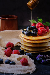 pancakes with berries and honey on dark background