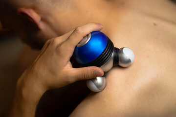 a man gives himself a massage with a purple and blue hand massager © Anastasiia