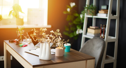 Well-organized workspace with a desk featuring a vase of flowers, office supplies, and soft sunlight streaming through the window. The bookshelf and greenery create a peaceful, productive atmosphere