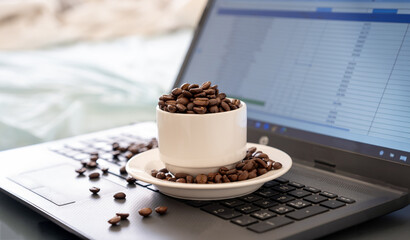 Cup of coffee that full of coffee beans on laptop background with rim light represents working...