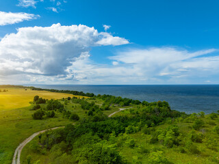 Obraz premium Aerial view of calm and wild Saka beach with a clear blue water on a cloudy summer day. Beautiful yellow and green fields and countryside road. Saka, Ida Viru county, Estonia. Selective focus.