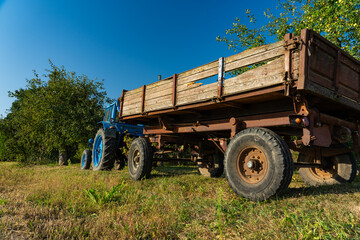 Obraz premium A blue, old tractor with a trailer stands near a field in the village. Morning