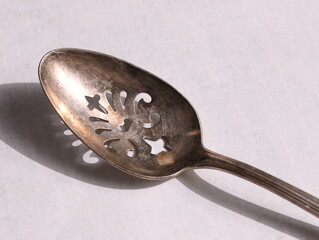 Tarnished silver spoon with ornate cut out pattern.