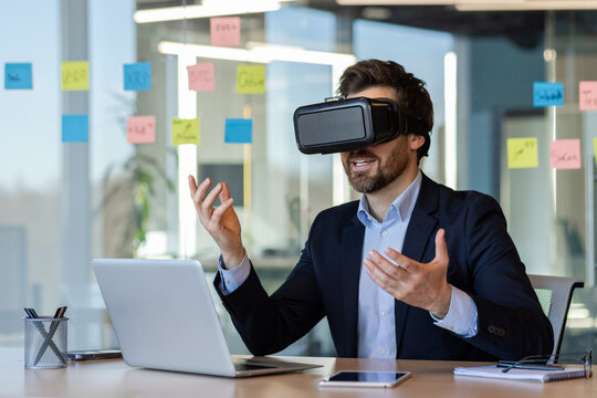 Businessman immersed in virtual reality while working in modern office setting. Engaging with technology using VR headset for innovative business solutions.