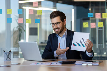 Businessman presenting data analysis in modern office setting. Smiling professional using laptop...