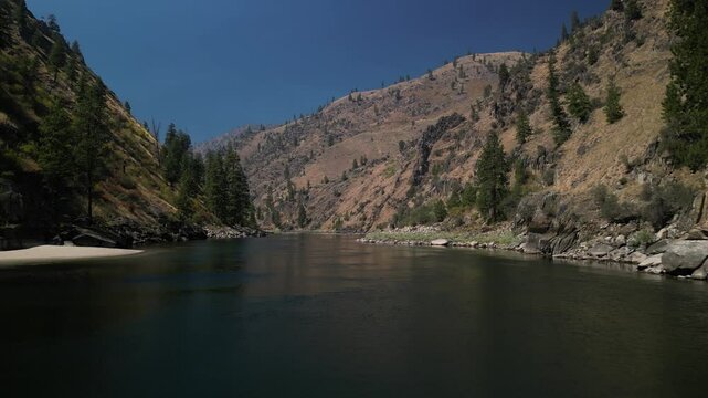 Low aerial above Salmon River on sunny day beneath dry mountain sides in summer
