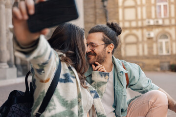Affectionate hipster couple flirting and taking selfies on city street