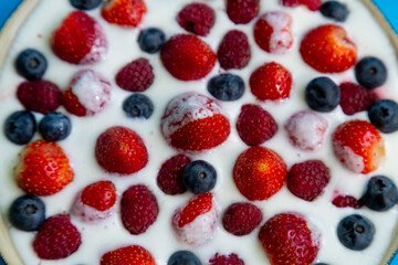 In a plate with freshly whipped cream juicy berries strawberries raspberries and blueberries close-up