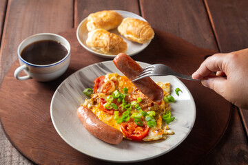 Eggs with tomatoes and sausage in a plate on the table of coffee and a croissant of sausage
