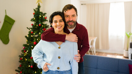 Joyful couple embraces near the holiday tree, spreading love and happiness in their warm home....
