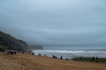 Tourists at Charmouth Beach collecting fossils on a cloudy and cold day by the English Channel, Dorset