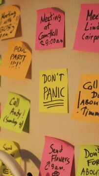 Vertical video. Hand of man placing vibrant paper with inscription Dont panic to a wall with lots of colorful sticky notes. Time organization and planning concept