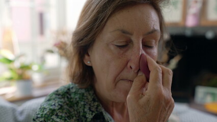 Close-up of an elderly woman applying makeup with a sponge, focused and detailed, in a brightly lit living room, showcasing self-care and daily beauty routine