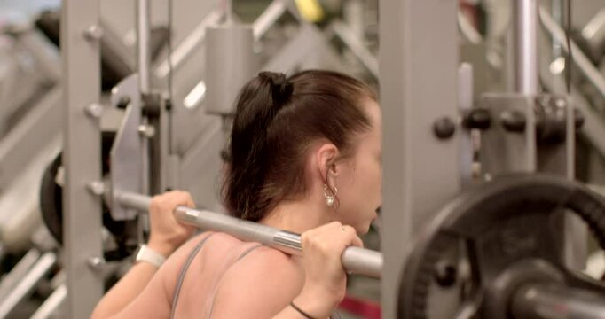 A young woman is performing barbell squats as part of her strength training routine at a modern sport center She raises and lowers the barbell on her shoulders.