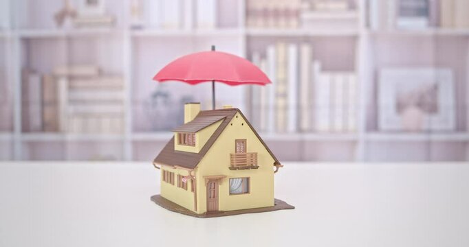 Protection from mortgage foreclosure and land contract forfeiture, business mortgage loan and real estate property insurance concept :  Red umbrella covers or protects a residential home model.