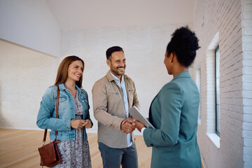 Happy real estate buyers shaking hands with black female agent during open house day.