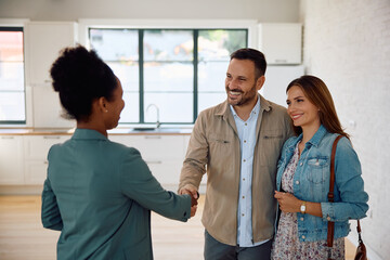 Happy man shaking hands with real estate agent while buy new home with his wife.
