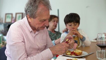 Grandfather peeling apples with his grandson at the table, while the grandmother looks on, creating a warm family bonding moment over a shared activity