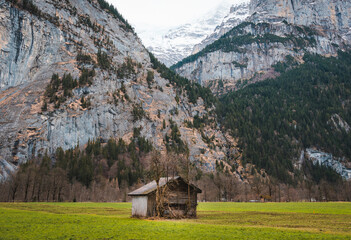 A solitary wood cabin in the valley of Lauterbrunnen, Switzerland. Mountains loom in the background.