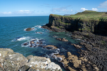 A rocky bay next to some coastal cliffs in Ireland. The sea is calm and sky is blue.