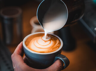 A barista pouring steamed milk into a coffee, creating some swirls of latte art. 