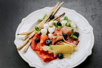 Italian antipasto platter with cured meats, cheese, olives, breadsticks, and fresh herbs 