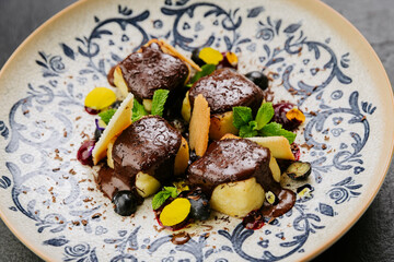 Chocolate-covered gourmet dessert with fresh mint, biscuit shards, and berries on a decorative plate