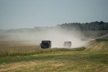 Fototapeta premium a pair of British army MAN SV4x4 utility trucks creating a dust cloud on an unmade road