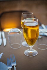 Blond golden beer served in a drinking glass on a served silverware table on brown palette, close up still
