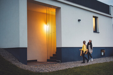 Fototapeta premium Mother and daughter coming home from a shopping together at dusk, with warm smart light illuminating the entrance. Enjoy spending time together. Holding bags with new clothes and shoes.