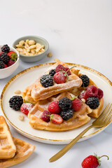 Belgian waffles decorated with strawberries, raspberries, blackberries and sprinkled with powdered sugar on a light background.