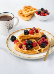 Belgian waffles decorated with strawberries, raspberries, blackberries and a cup of cocoa on a light background.