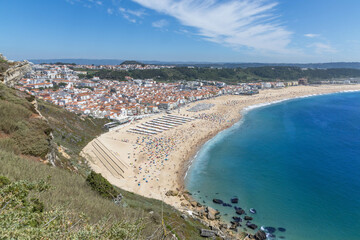 Nazaré sand beach and hills on a summer day with a beach full of people at Nazare Portugal.