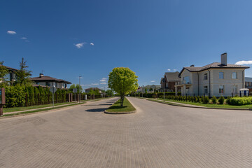 Novorizhsky township 03.06.2023 : A serene residential street with a central tree surrounded by houses on a sunny day, showcasing peaceful suburban living