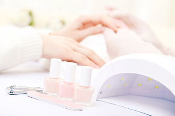 Manicurist making manicure for client with lamp and bottles
