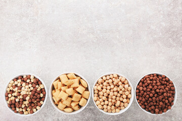 Various corn flakes in bowls on grey background