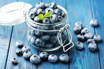 Tasty blueberries with mint leafs in glass jar on blue wooden background