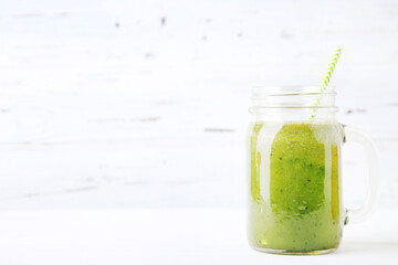 Green smoothie in glass jar on white wooden background