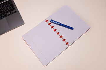 An overhead shot of an open notebook with a blue fountain pen and part of a laptop on a clean, light-colored desk.