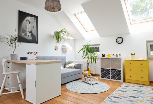 Cozy interior of room child with white color on the wall and yellow color in decor. Room in the attic with sofa, desk with chair and carpet in modern design on wooden floor. Scandinavian concept.	