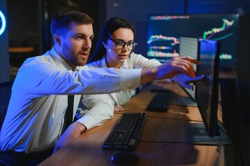 Team of stockbrokers are having a conversation in a dark office with display screens