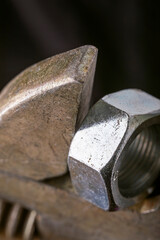 Adjustable wrench holding metal nut on dark background. Macro shot of tool and hardware for construction and repair.