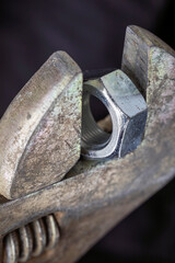 Adjustable wrench holding metal nut on dark background. Macro shot of tool and hardware for construction and repair.